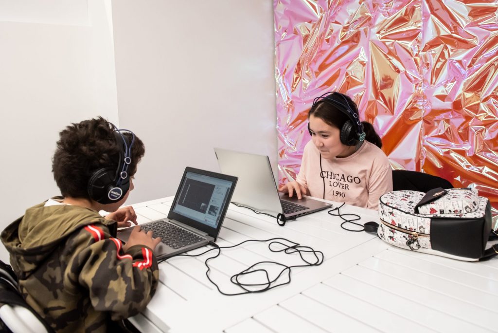 Two young people wearing headphones sitting at laptops