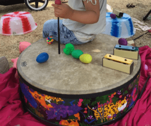A child sitting on a drum, with musical instruments scattered around.