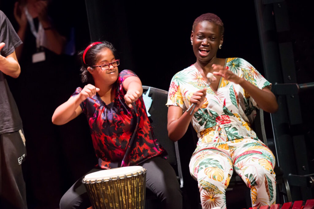 two people singing and with hands in the air, with one drum