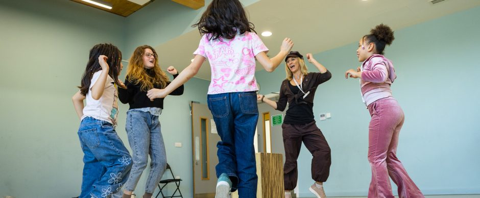 A group of children dancing and smiling with teachers leading.